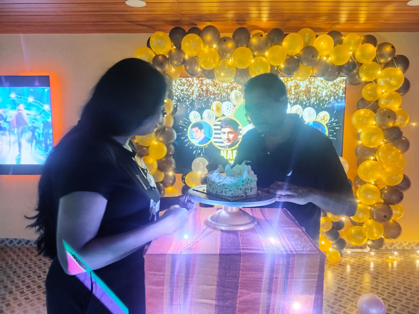 Cake-cutting moment in front of a balloon arch and a personalised birthday screen