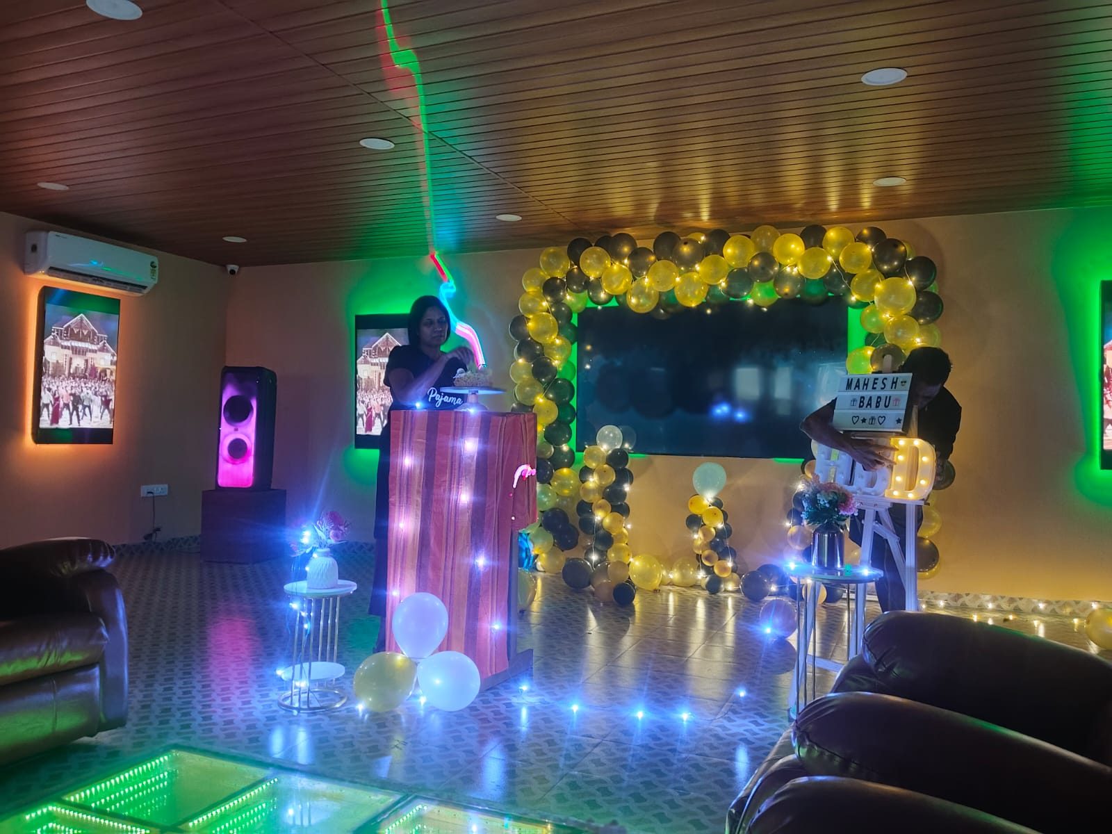 Birthday party in the hall — neon-lit screens, balloon arch, glowing HBD letters and LED floor