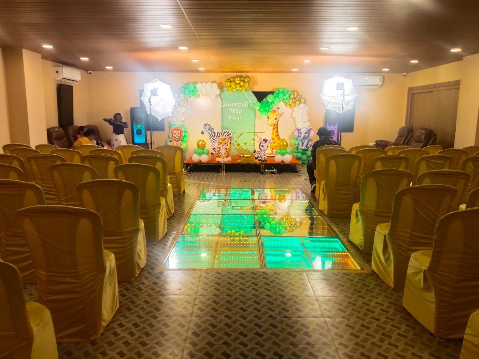Kids’ jungle-theme birthday stage at the end of a glowing LED aisle, with guest seating