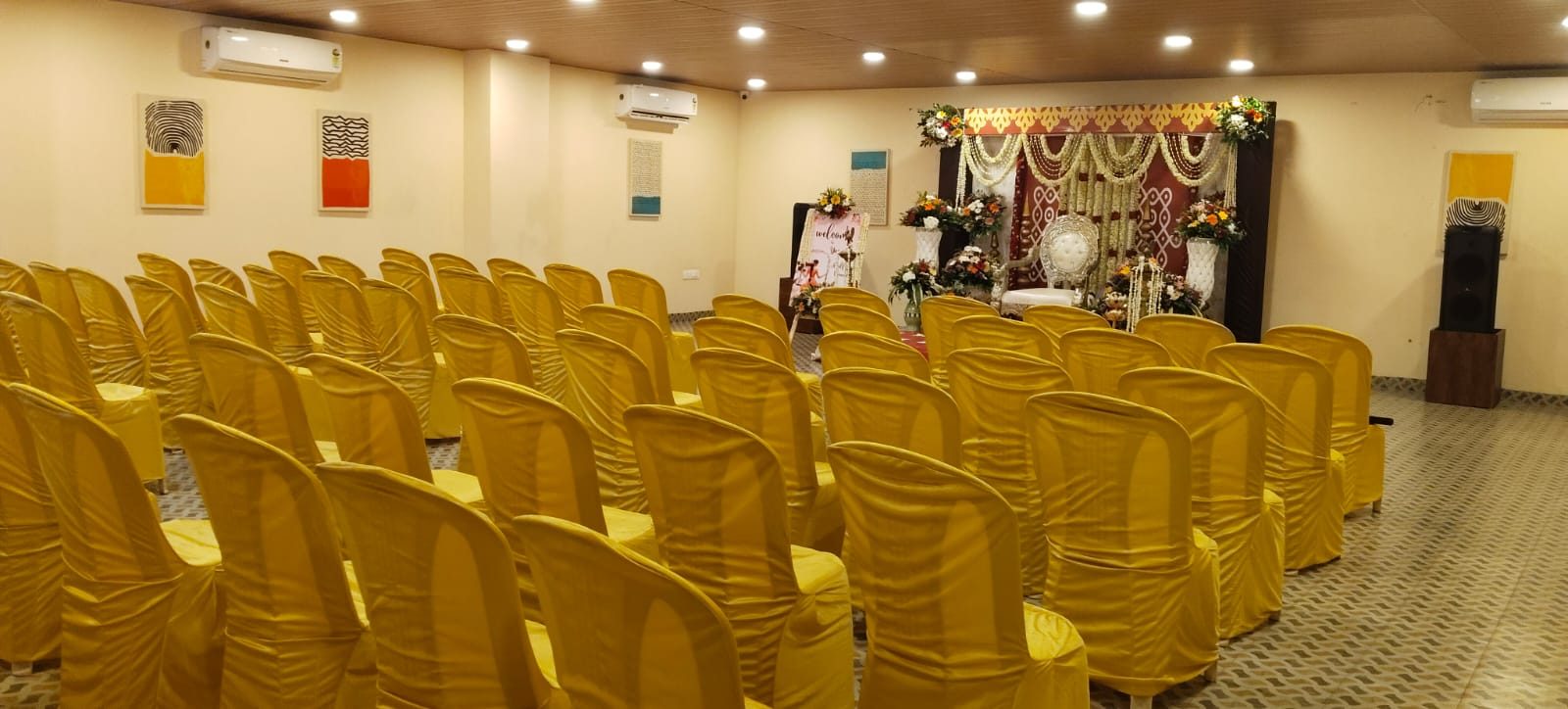 Function hall set up for a half-saree ceremony — floral stage and rows of covered chairs